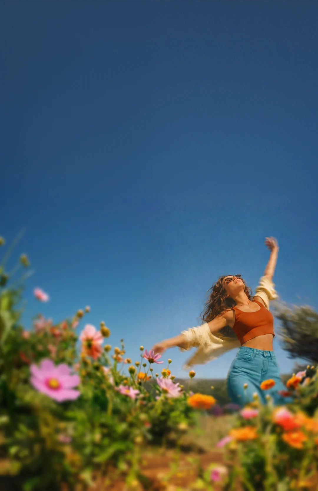 Woman in an orange top moving through colourful flowers beneath a blue sky