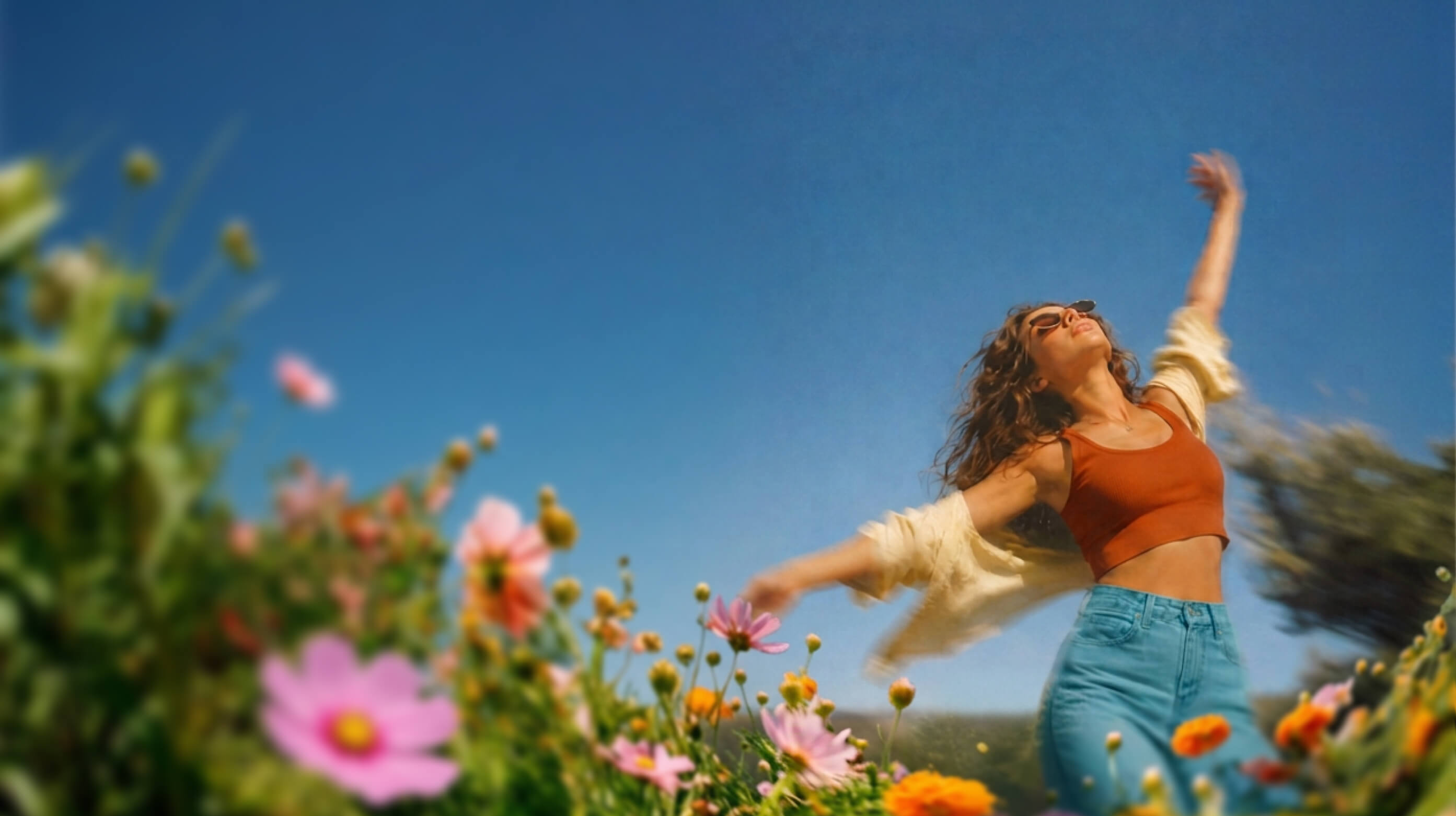 Woman in an orange top moving through colourful flowers beneath a blue sky